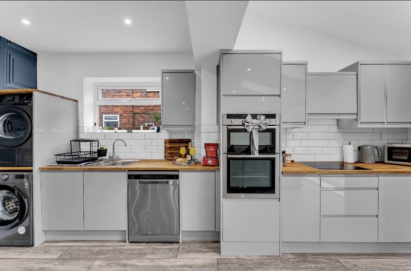 Modern kitchen with white cabinetry, wooden countertops, stainless steel appliances and brick accent wall