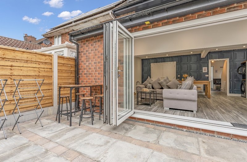 Modern patio area with bi-fold doors opening to living room, wooden fencing and garden furniture