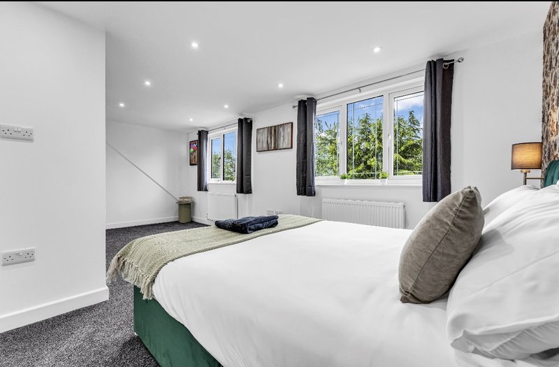 Bright bedroom with double bed, grey cushion, windows overlooking garden, recessed lighting