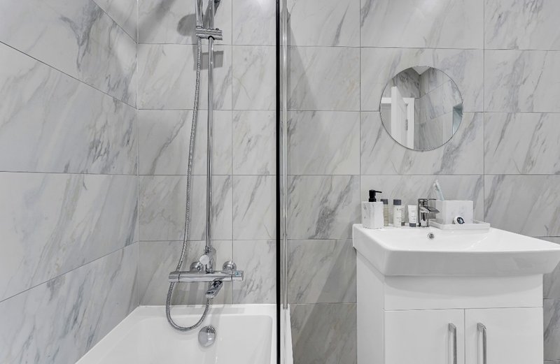 Modern bathroom with marble tiles, shower enclosure, white vanity sink and round mirror