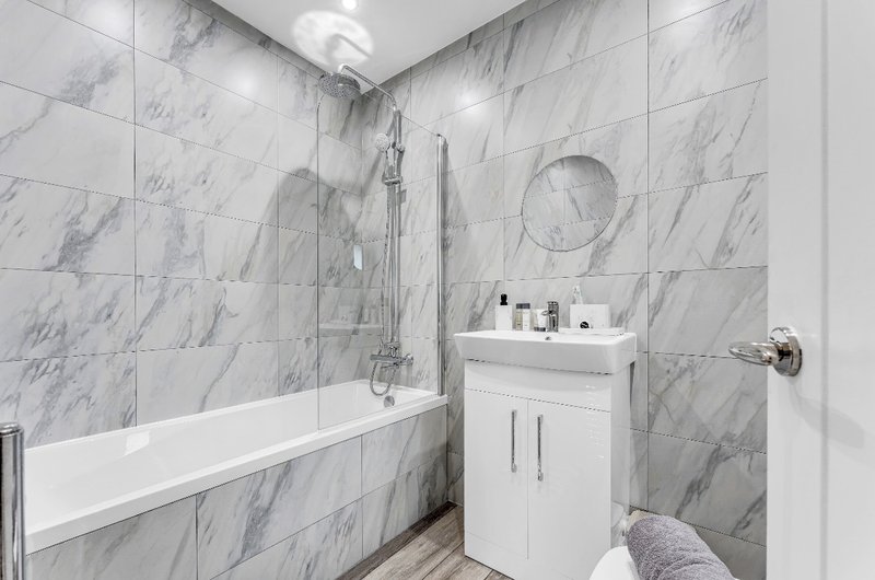 Modern bathroom with marble-effect tile walls, white bathtub, vanity sink and chrome fixtures