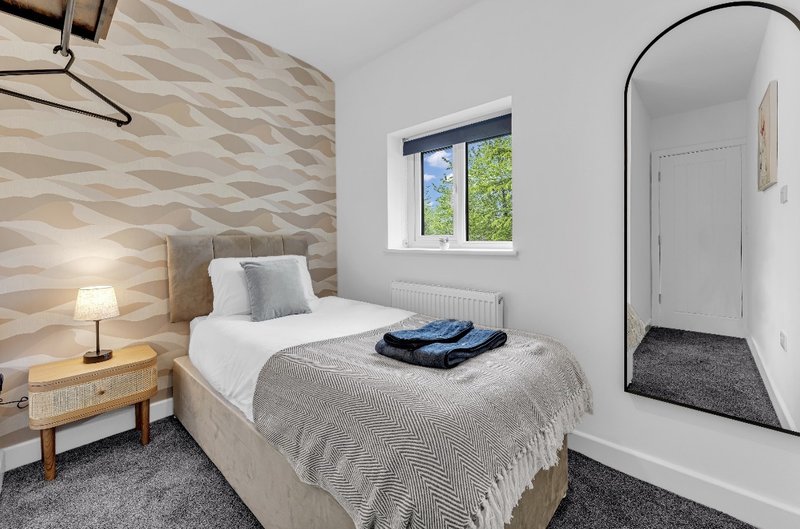 Modern bedroom with single bed, geometric headboard, bedside lamp and arched mirror