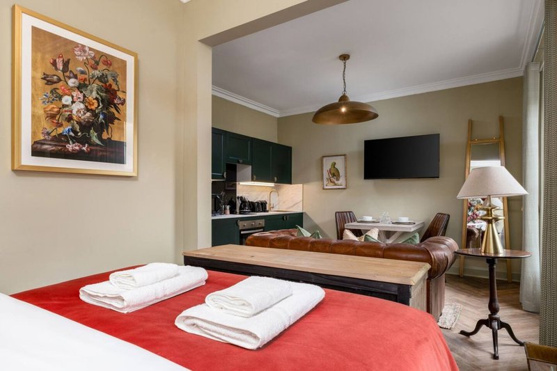 Modern studio bedroom with red bedding, kitchenette, TV, and open-plan living area