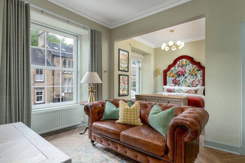 Living room with brown leather Chesterfield sofa, cushions, window with curtains, and wall art