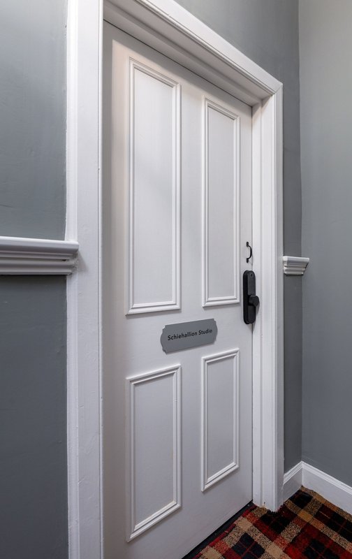 White panelled door with black handle and nameplate, grey walls, tiled floor