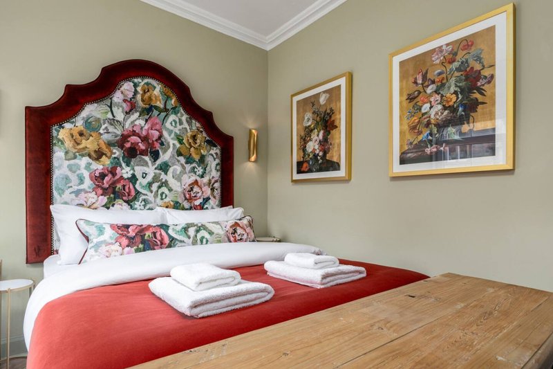 Bedroom with floral upholstered headboard, red throw, white pillows, and framed botanical artwork