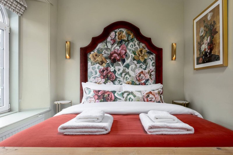 Bedroom with red bed, floral headboard, white pillows and folded towels
