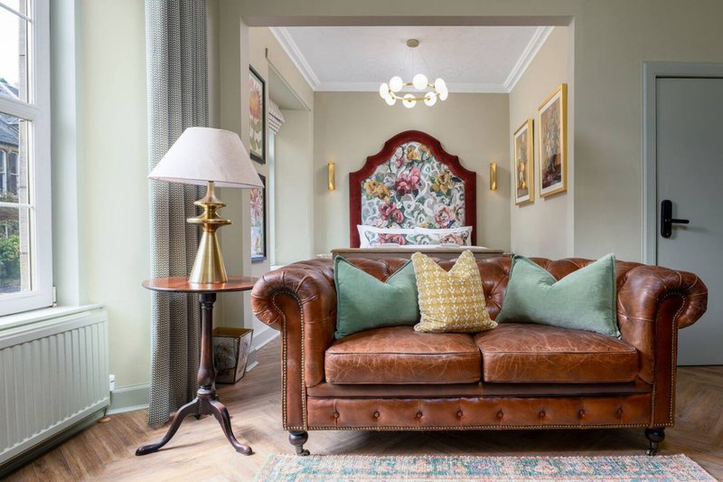 Elegant living room with brown leather Chesterfield sofa, decorative pillows, lamp, and period furnishings