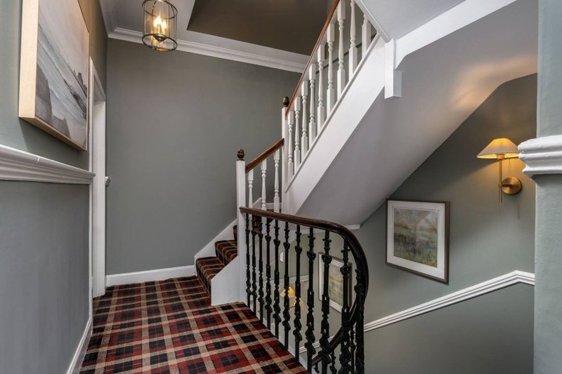 Hallway and staircase with black railing, plaid carpet, gray walls and pendant lighting