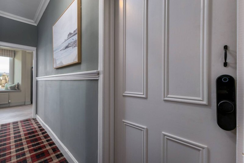 Hallway with gray paneled walls, framed artwork, tartan runner rug and door