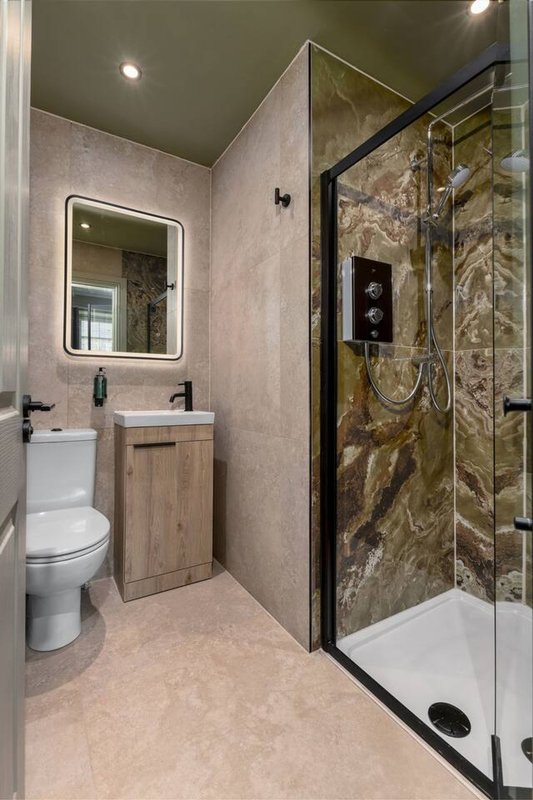 Modern bathroom with walk-in shower, vanity sink, illuminated mirror and beige tiling