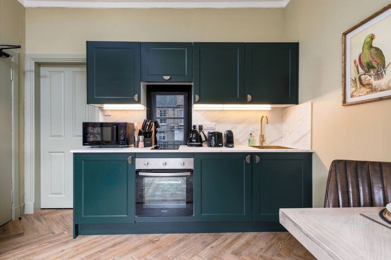 Modern kitchen with dark teal cabinets, white countertop, built-in oven and wooden flooring