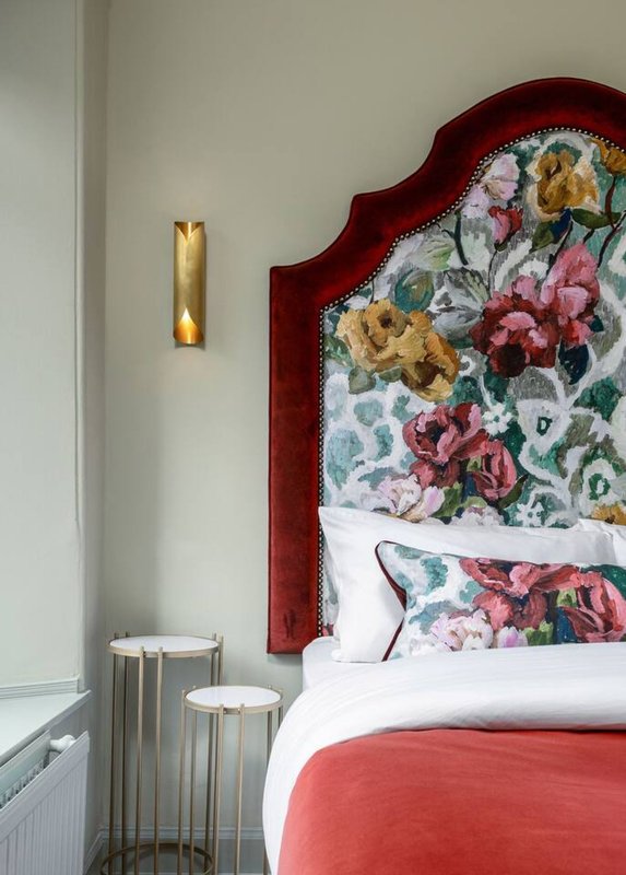Bedroom with red upholstered headboard, floral patterned bedding, white nightstands, and gold wall sconce