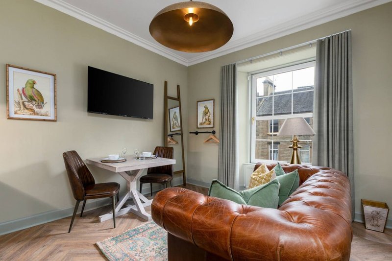Modern living room with cognac leather sofa, dining table, wall-mounted TV and large windows