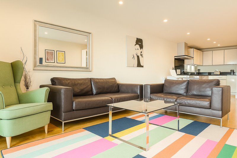 Contemporary living room with brown leather sofas, colorful geometric area rug, glass coffee table and green armchair