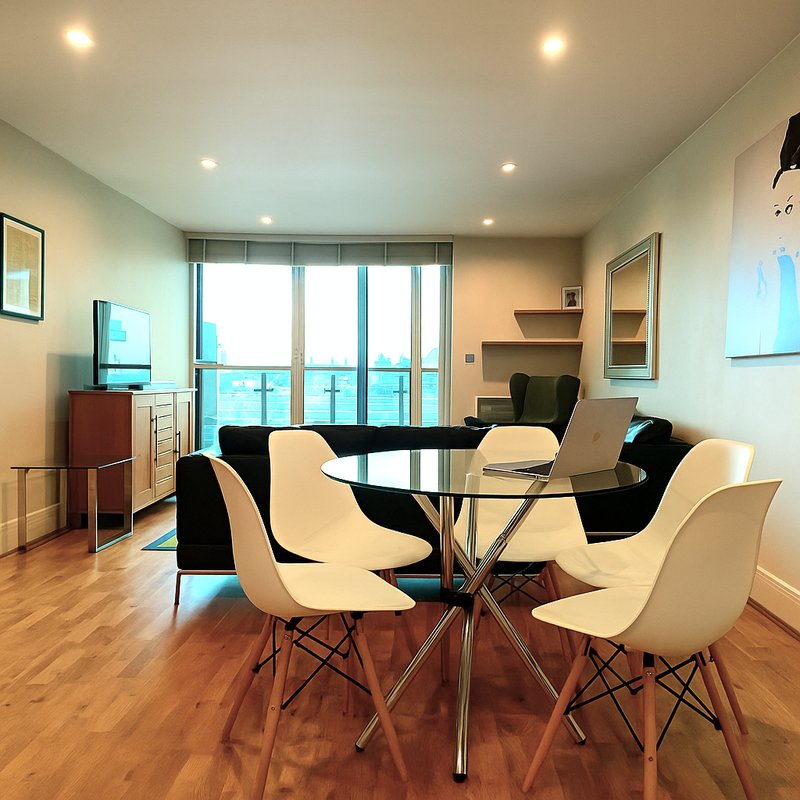 Modern dining area with round glass table, cream and black chairs, wooden floor, and floor-to-ceiling windows