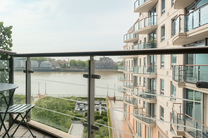 Riverside apartment balcony with glass railing overlooking water and landscaped grounds