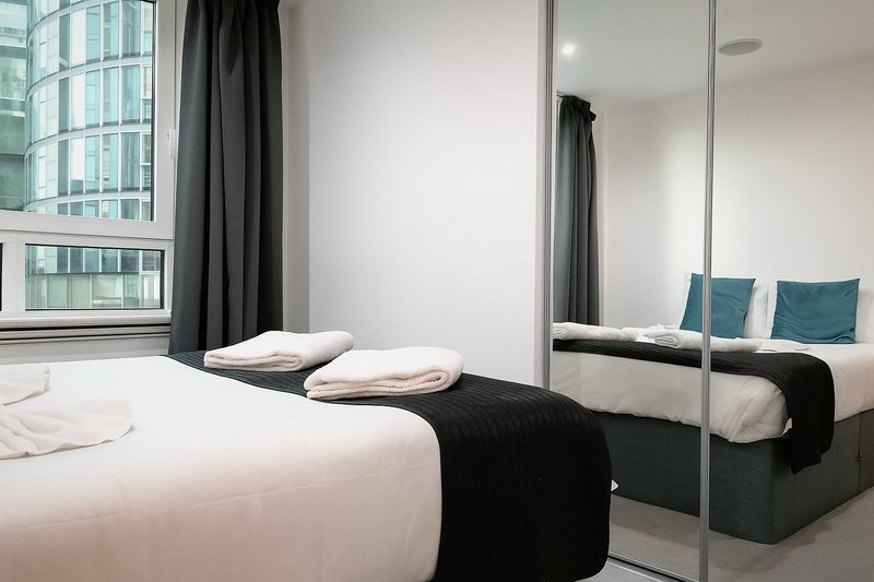 Modern bedroom with double bed, mirrored wardrobe, and city view from large window
