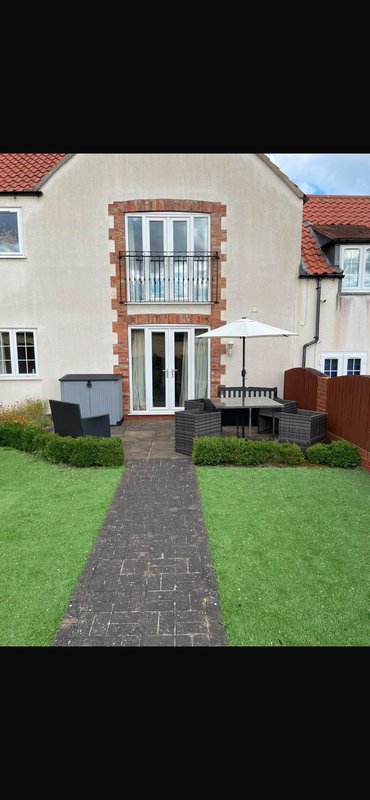 Cream and brick cottage exterior with paved pathway, green lawn, and patio seating area
