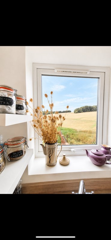 Kitchen windowsill with dried flowers, storage jars, and view of countryside fields