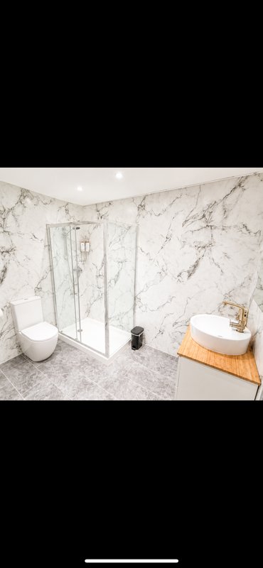 Modern bathroom with marble walls, white toilet, glass shower enclosure and wooden vanity