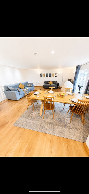 Open-plan living room with wooden dining table, blue sofa, hardwood flooring and natural light
