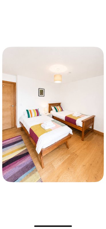 Bright bedroom with two single beds, wooden furniture, colorful rug and wooden flooring