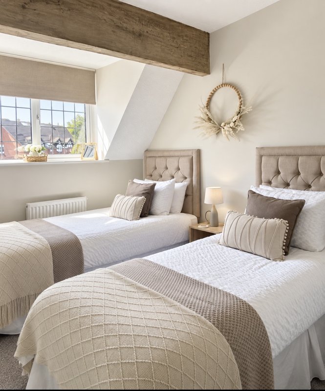 Modern bedroom with two single beds, neutral bedding, upholstered headboards and sloped ceiling