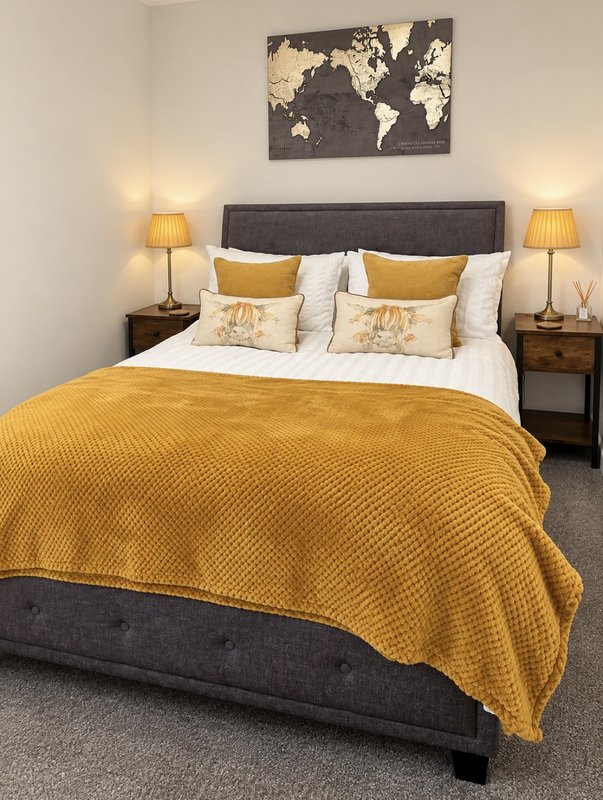 Bedroom with double bed, yellow bedding, grey headboard, bedside lamps and world map wall art