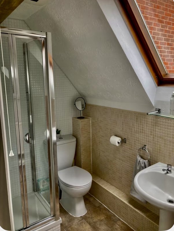 Attic bathroom with shower cubicle, toilet, sink, and beige tile walls