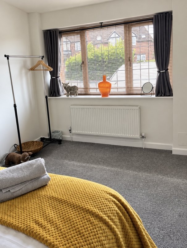 Bright bedroom with double bed, grey carpet, large window with black curtains and windowsill decor