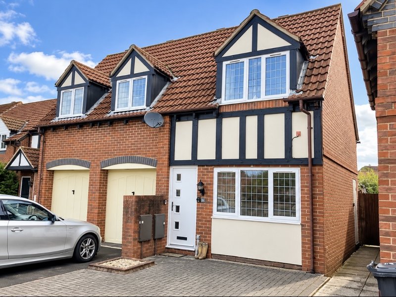 Brick and timber-framed house exterior with driveway, garage doors and parked car