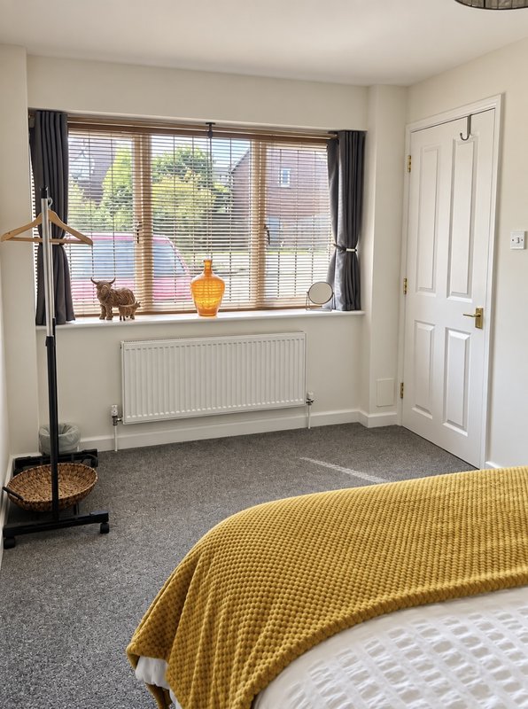 Bright bedroom with double bed, large window, coat stand, and radiator heater
