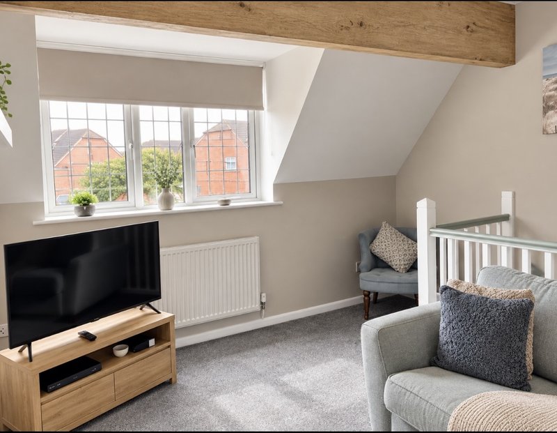 Bright attic bedroom with TV, wooden beams, window views, crib and upholstered chair