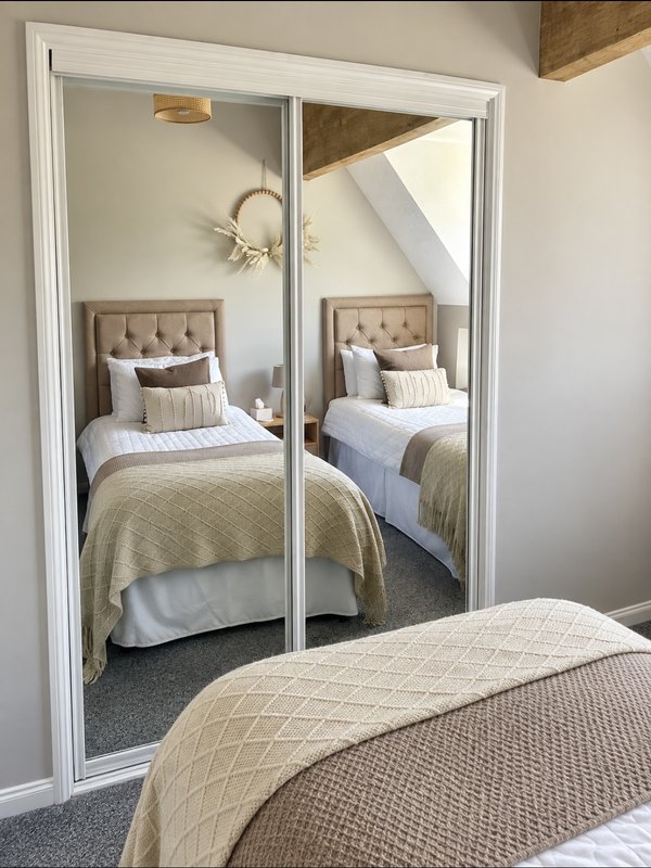 Bedroom with mirrored wardrobe doors reflecting twin beds with upholstered headboards and neutral bedding