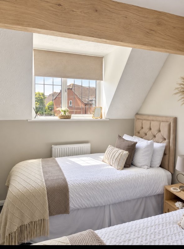Bright attic bedroom with double bed, beige headboard, and skylight window overlooking brick houses
