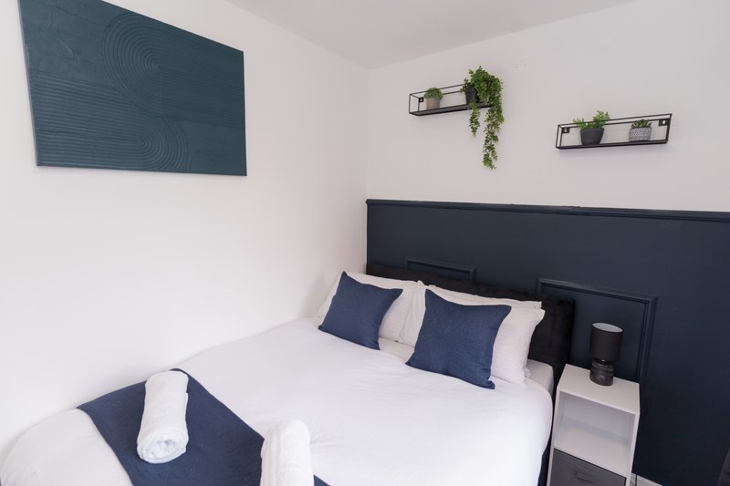 Modern bedroom with double bed, navy headboard, white bedding, and decorative wall shelves