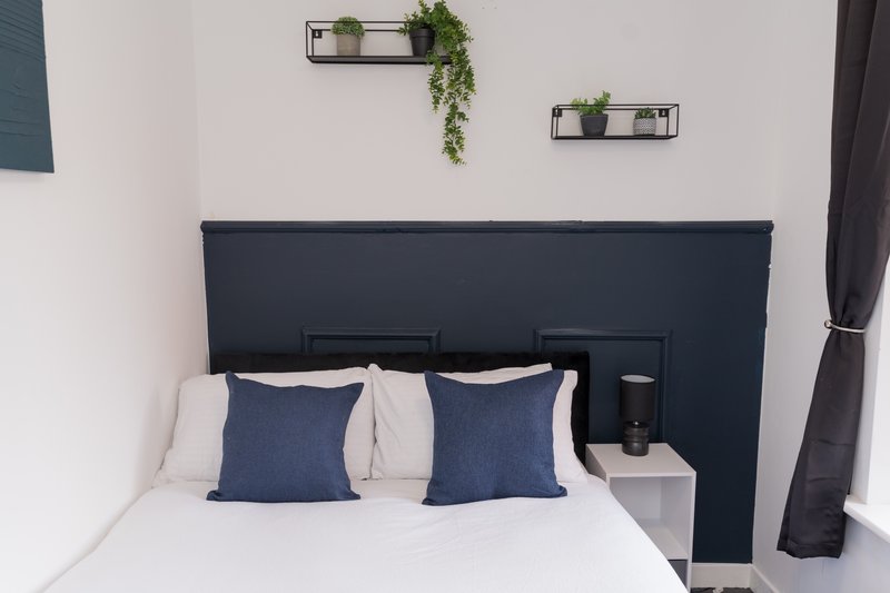 Modern bedroom with dark headboard, white bedding, blue cushions and wall-mounted plant shelves