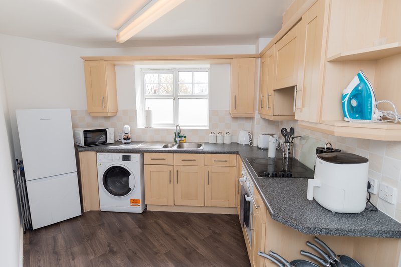 Modern kitchen with light wood cabinets, white appliances, dark countertops and wood flooring
