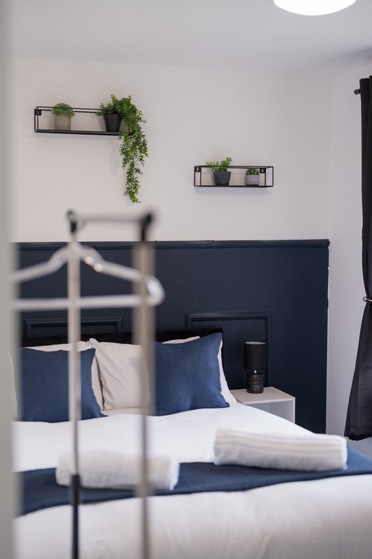 Modern bedroom with navy headboard, white bedding, blue pillows and wall-mounted plant shelves