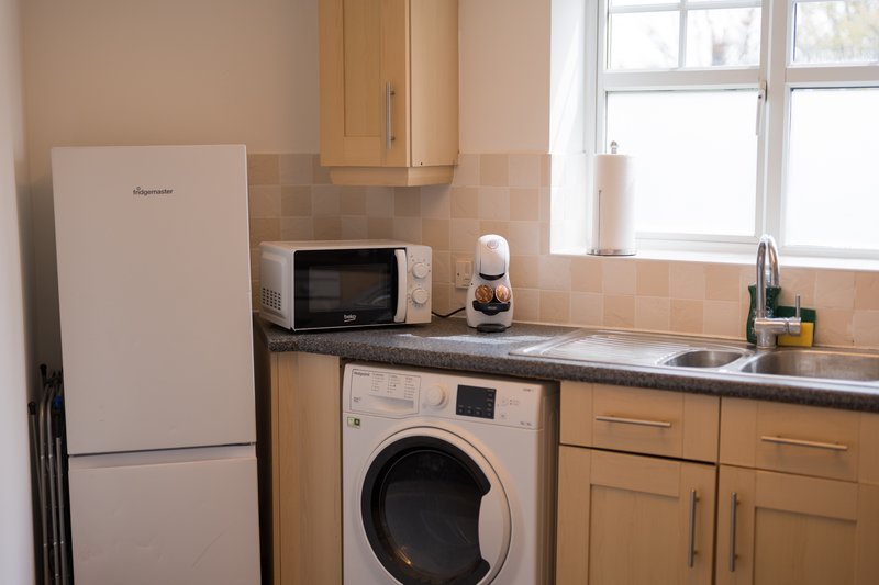 Compact kitchen with wooden cabinets, refrigerator, washing machine, microwave and window