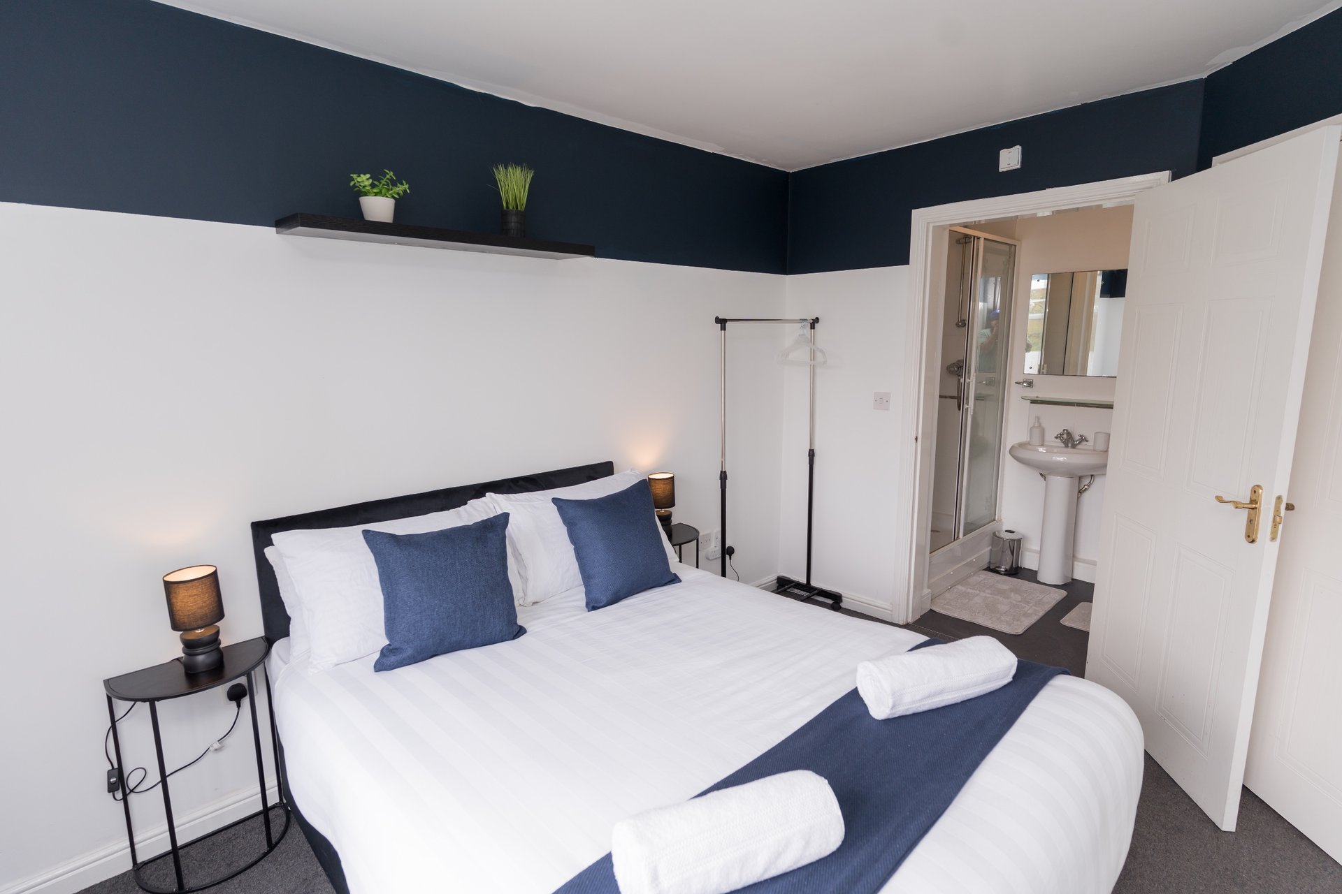 Modern bedroom with double bed, dark blue headboard, white bedding, and ensuite bathroom visible