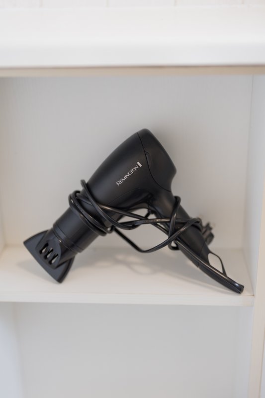 Black hair dryer with cord coiled on white shelf