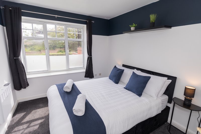 Modern bedroom with double bed, navy bedding, large window and dark accent wall