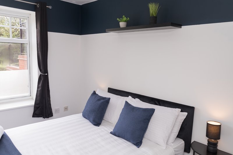 Modern bedroom with double bed, blue cushions, dark headboard and two-tone walls