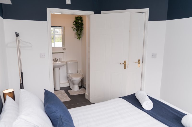 Modern bedroom with double bed, en-suite bathroom visible through open door, navy and white décor
