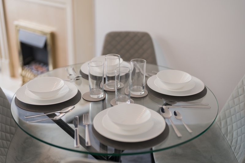 Round glass dining table set with white plates, glasses, cutlery and napkins