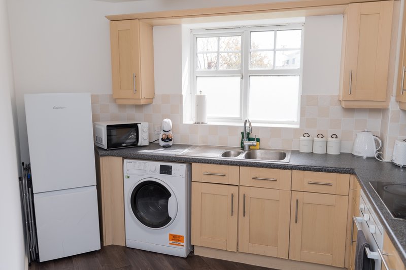 Kitchen with wooden cabinets, white fridge, washing machine, sink and window