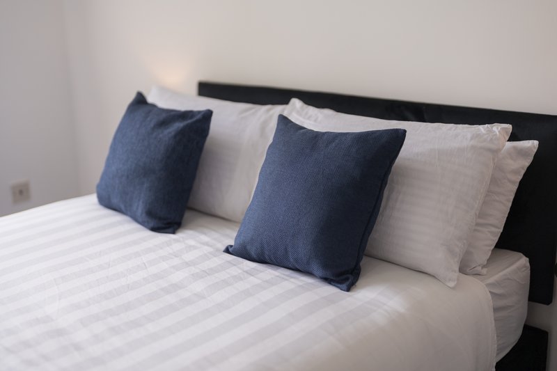 Bed with white striped bedding, black headboard, and blue and cream cushions