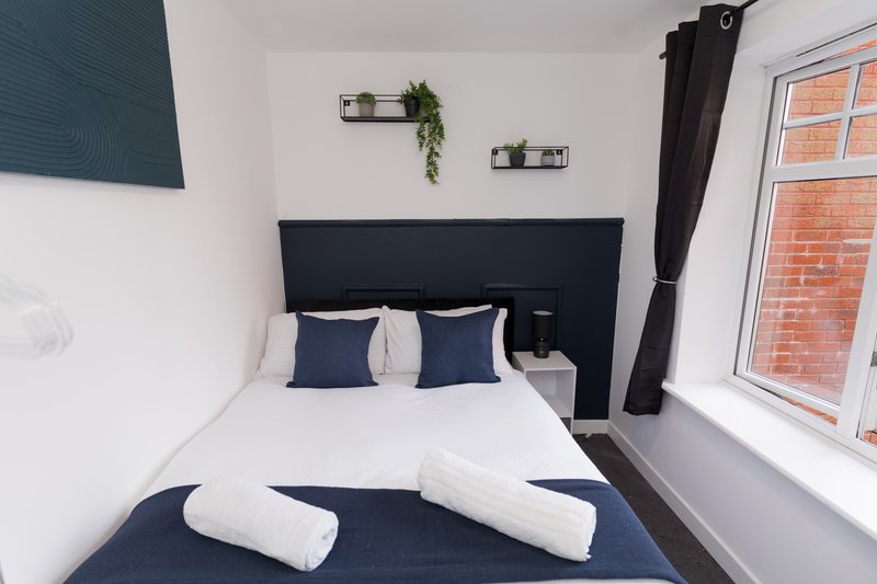 Compact bedroom with double bed, navy headboard, white bedding, and window overlooking brick building